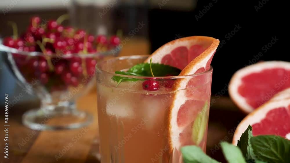 Currant falls into grapefruit lemonade with ice in a glass close up in slow motion. Making a summer refreshing drink Currant falls into grapefruit lemonade with ice in a glass close up in slow motion. Making a summer refreshing drink