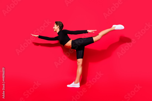 Full length body size profile side view of attractive cheerful girl stretching keeping balance isolated over bright red color background