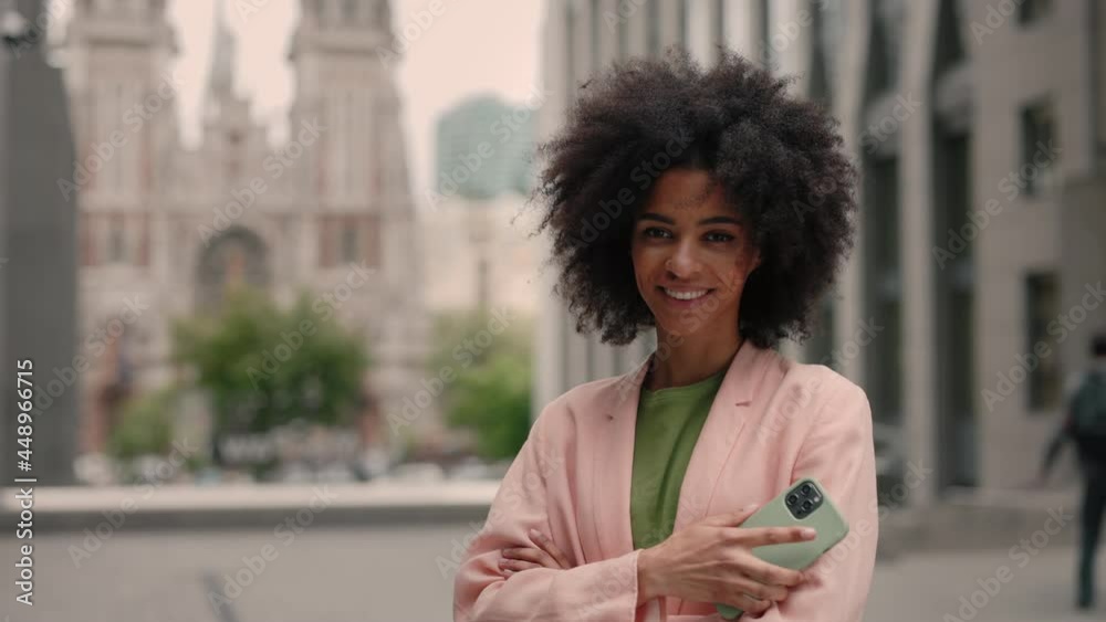Young business woman with smartphone in her hand looking to the camera standing near business centre. People portraits and technology concept. Young business woman with smartphone in her hand looking to the camera standing near business centre. People portraits and technology concept.