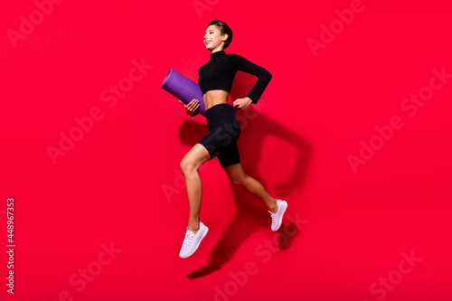 Profile photo of runner cheerful lady jogging carry mat carpet wear black cropped top isolated red color background © deagreez
