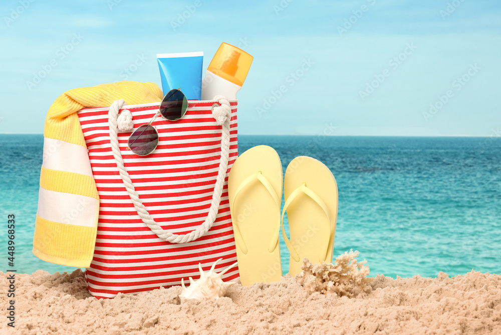 Stylish bag with different accessories on sandy beach near ocean Stylish bag with different accessories on sandy beach near ocean