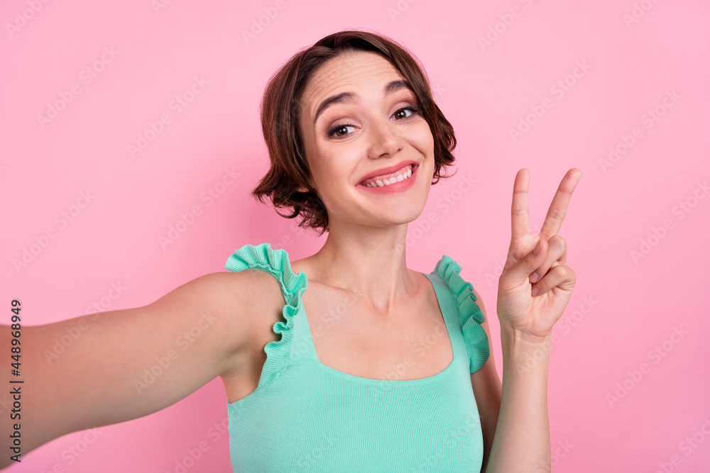 Self-portrait of attractive cheerful funky girl showing v-sign having fun isolated over pink pastel color background Self-portrait of attractive cheerful funky girl showing v-sign having fun isolated over pink pastel color background