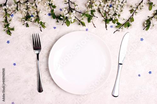 Festive table setting with cutlery, apple blossomand and forget-me-not flowers on a light marble background.