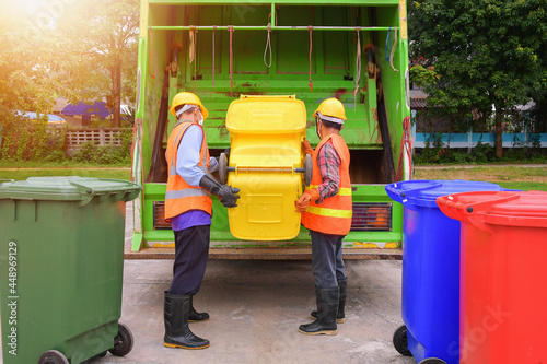 Two dustmen standing by a dustbin lorry emptying wheelie bins, Thailand photo