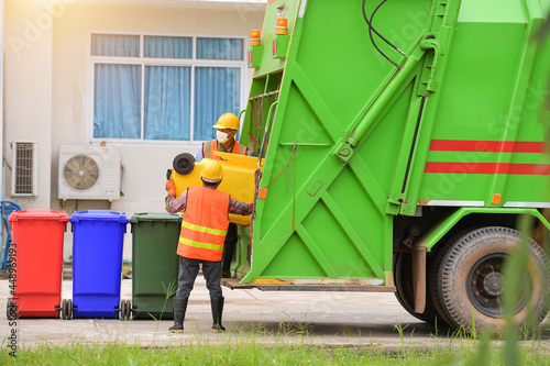 Two dustmen standing by a dustbin lorry emptying wheelie bins, Thailand