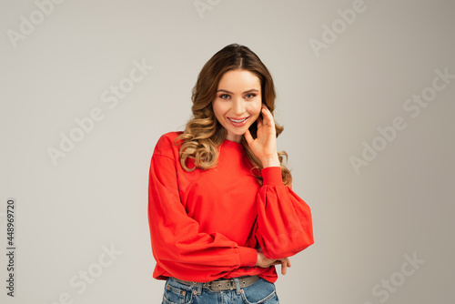 happy woman in sweatshirt looking at camera isolated on grey