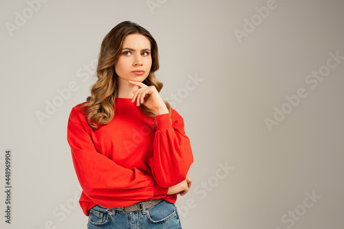 pensive woman in red sweatshirt looking away and thinking isolated on grey