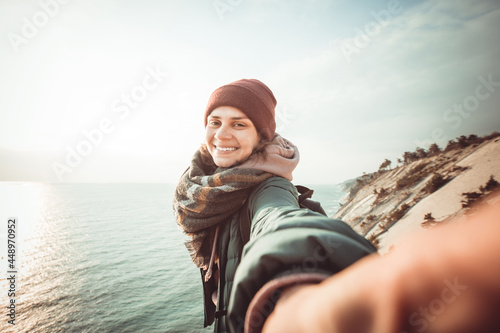 Happy woman traveler makes selfie on the background of the sea and sky. She is inspired and free. The weather is cold and sunny.