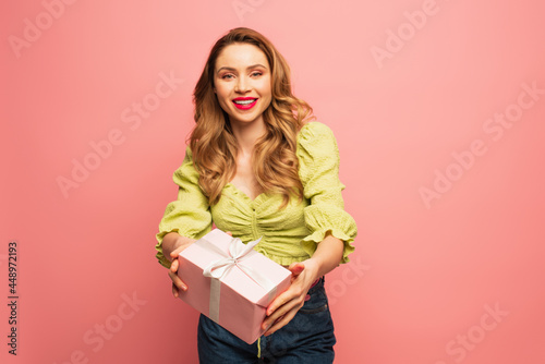 positive woman holding wrapped present isolated on pink