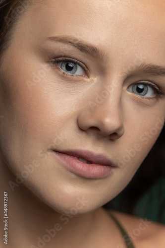 Close-up young beautiful adorable girl's face isolated over dark green studio background. Natural beauty, wellness, well-kept skin, herbal cosmetics concept