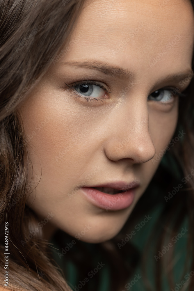 Close-up young beautiful adorable girl's face isolated over dark green studio background. Natural beauty, wellness, well-kept skin, herbal cosmetics concept