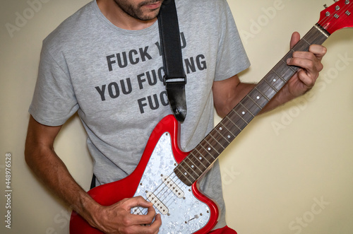Fotografi Young man with offensive t-shirt playing a red electric guitar.