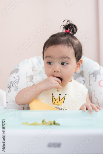 Cute Asian baby girl wearing  baby apron sitting on dining table eat broccoli by her self, Baby Led Weaning concept
