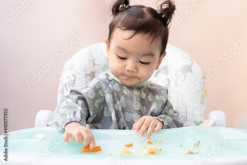 Cute Asian baby girl sitting on dining table practice eat food by her self, Baby-Led Weaning concept