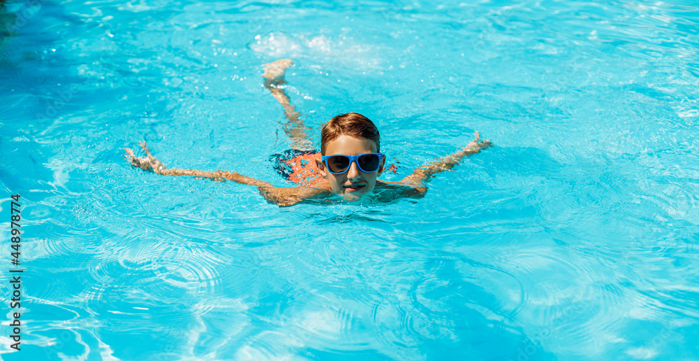 Little boy in sunglasses swimming in the pool having fun, Happy child playing in the pool, Summer vacation concept, Top portrait