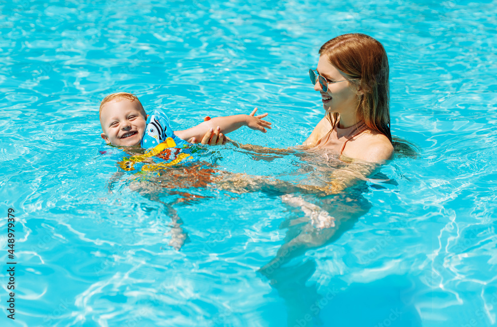 Happy family, mom and baby in inflatable vest swim and enjoy in the pool, have fun in the water on family vacation, Summer vacation