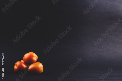 A few tomatoes are isolated on a dark and simple background. 