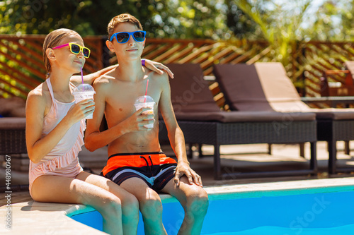 Happy cute kids, boy and girl drinking cocktails, relaxing sitting near the pool, happy summer, friendly family weekend concept