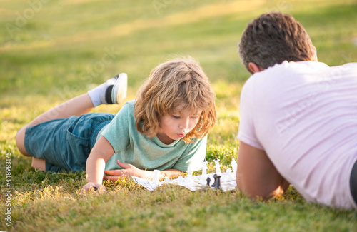 happy family of dad and son boy playing chess on green grass in park outdoor, strategic