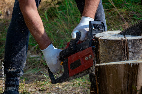 Unrecognizable male logger saws tree with hand held cordless chainsaw in forest. Chainsaw is in operation. Close-up of chain saw saw cutter in motion, sawdust flying on sides. Concept down trees. © Irina