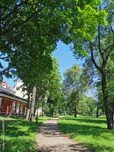 A path next to a beautiful old building in the Summer Garden of Kronstadt against the background of a blue cloudless sky