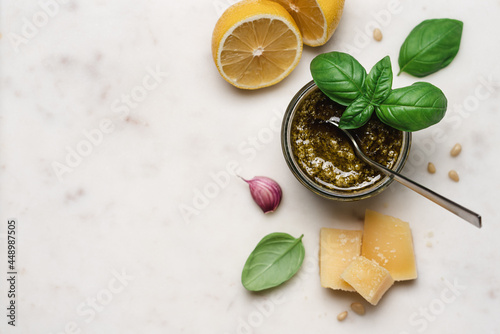 Pesto sauce in glass jar on marble background. Traditional ingredients for cooking. Basil, olive oil, lemon, parmesan cheese, pine nuts