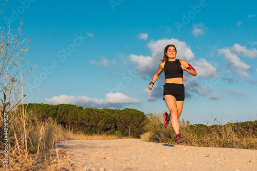 Front view of a caucasian young woman running and jumping in a mountain path during the golden hour.