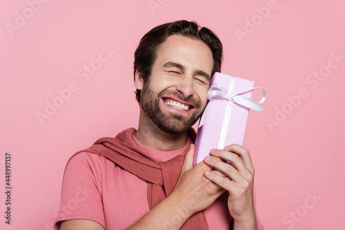 Happy man with closed eyes holding gift box isolated on pink