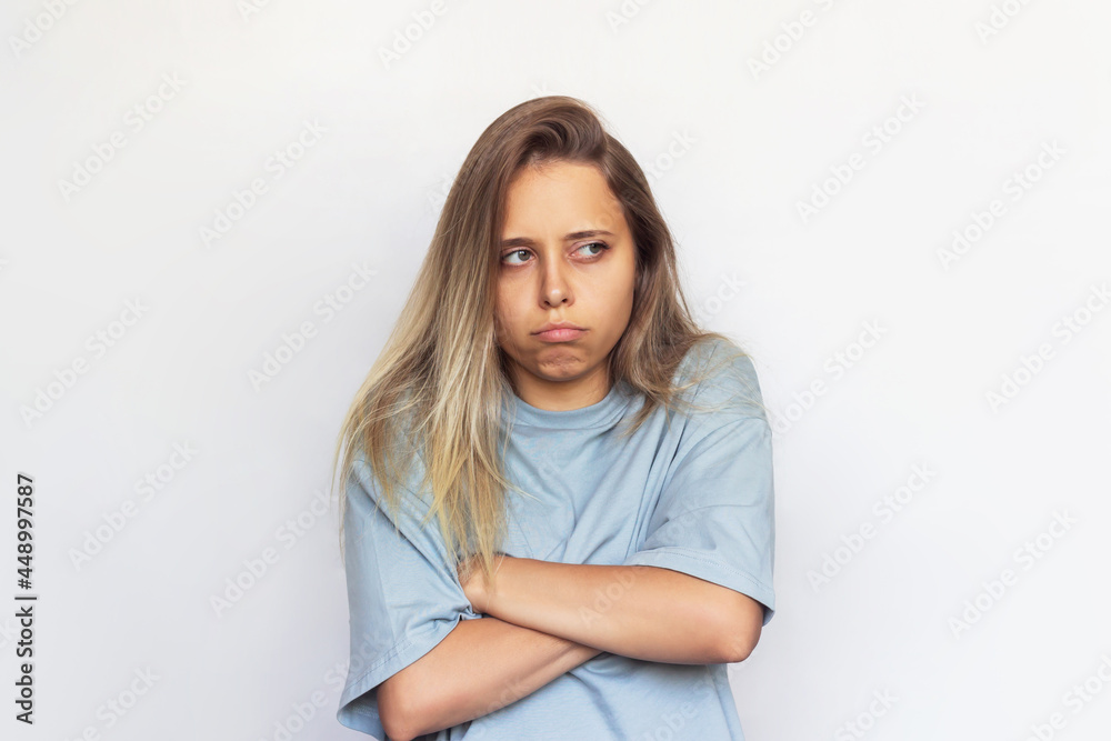 A young blonde beautiful upset offended woman in a gray t-shirt stands with her arms crossed on her chest and looks away with pouting lips isolated on a white background A young blonde beautiful upset offended woman in a gray t-shirt stands with her arms crossed on her chest and looks away with pouting lips isolated on a white background