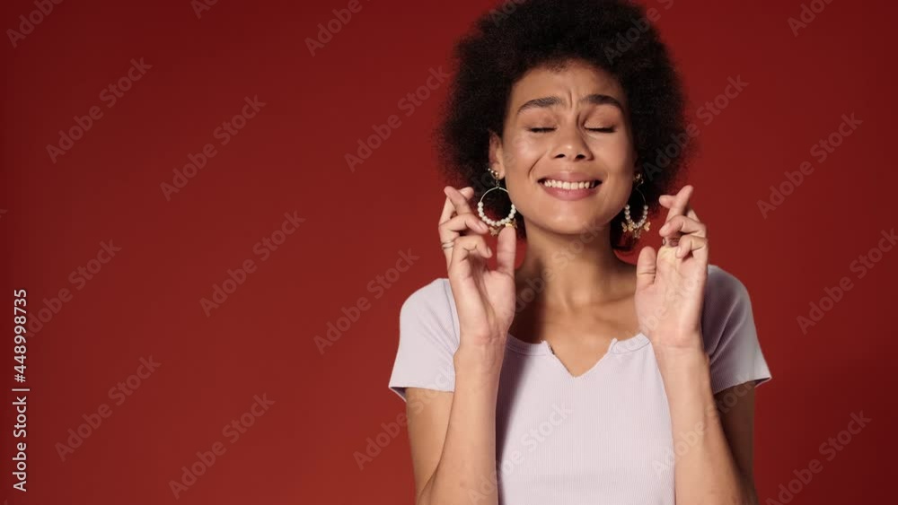 An african american woman crossing fingers while standing isolated over red wall in the studio An african american woman crossing fingers while standing isolated over red wall in the studio