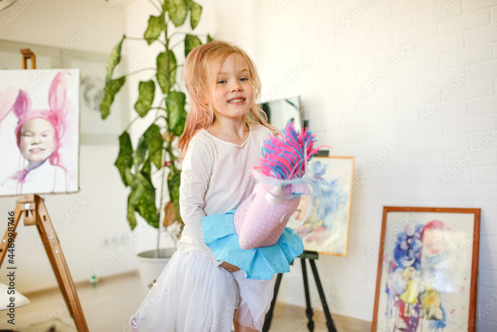 Funny european child toddler plays with a unicorn on a stick at home in a light real room