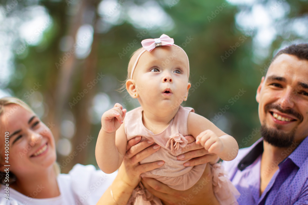 Fototapeta premium Husband, wife and their little daughter for a walk in the park. Happy dad and mom with one year old baby girl. Young family.