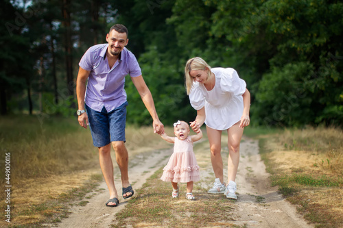 Husband, wife and their little daughter for a walk in the park. Happy dad and mom are walking through the woods with their one-year-old daughter.