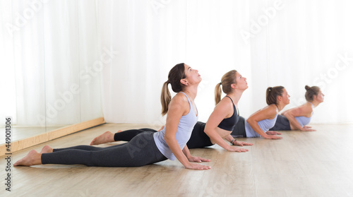 Group of young sporty sexy women in yoga studio, practicing yoga lesson with instructor, forming a line in asana pose. Healthy active lifestyle, working out indoors in gym