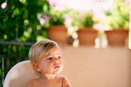 Serious child with a stained chin sits on a high chair on the balcony