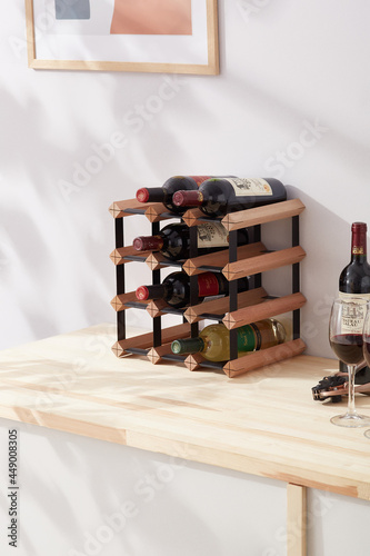Interior photo: stylish wine rack with bottles is located on the table near wine glasses. Wine shelf is made of wood and metal and designed for 12 bottles. 