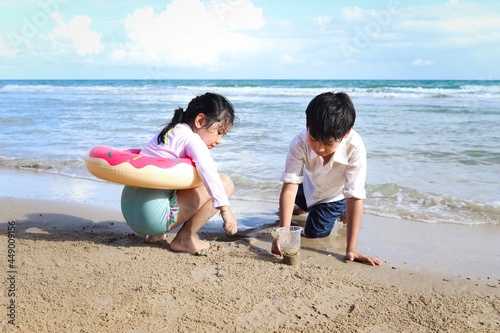 Two cute kids boy and girl having fun together on sandy summer beach with blue sea, happy childhood friend playing with sand on tropical beach, brother and sister spending time on family vacation. © Stella