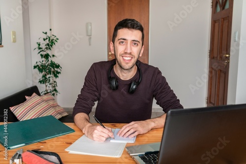 Man studying from home and looking at the camera with a big happy smile.