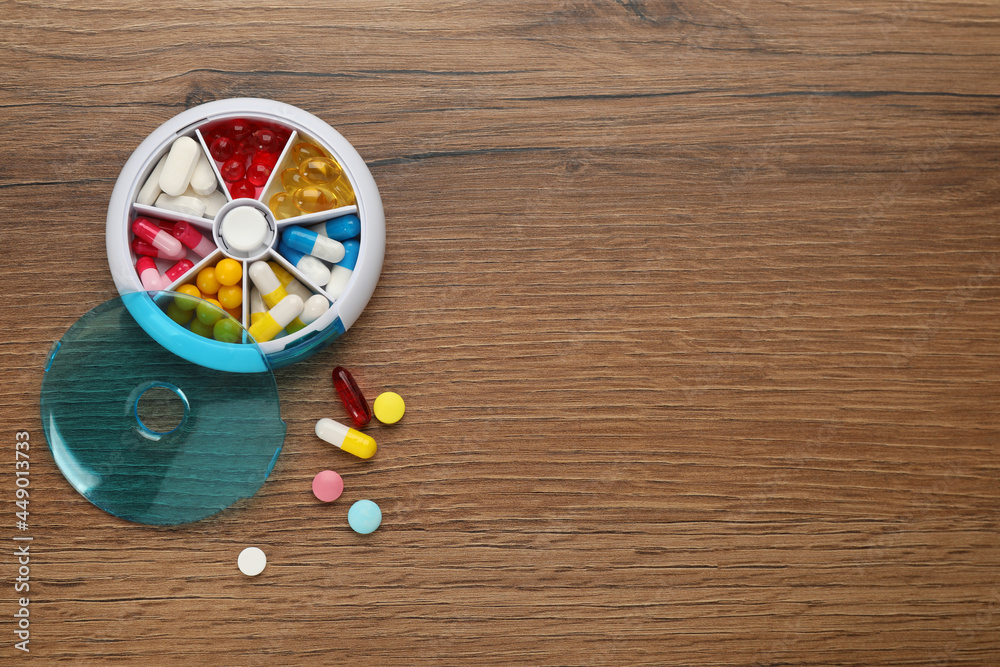 Plastic box with different pills on wooden table, flat lay. Space for text Plastic box with different pills on wooden table, flat lay. Space for text