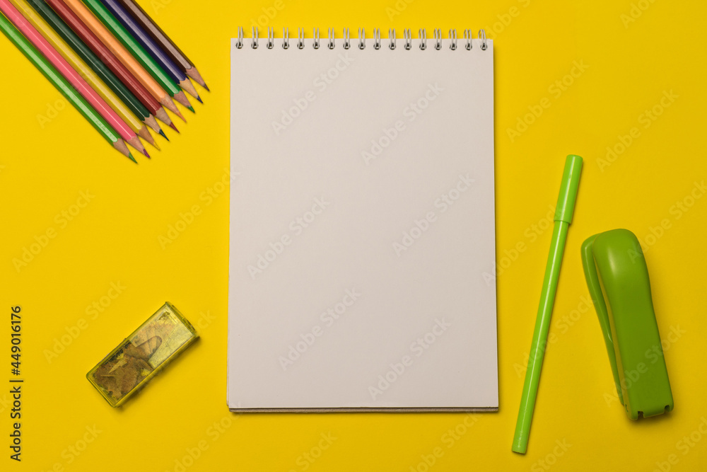 Office supplies and a blank white notepad sheet for your text on a yellow background. School supplies. Office supplies and a blank white notepad sheet for your text on a yellow background. School supplies.
