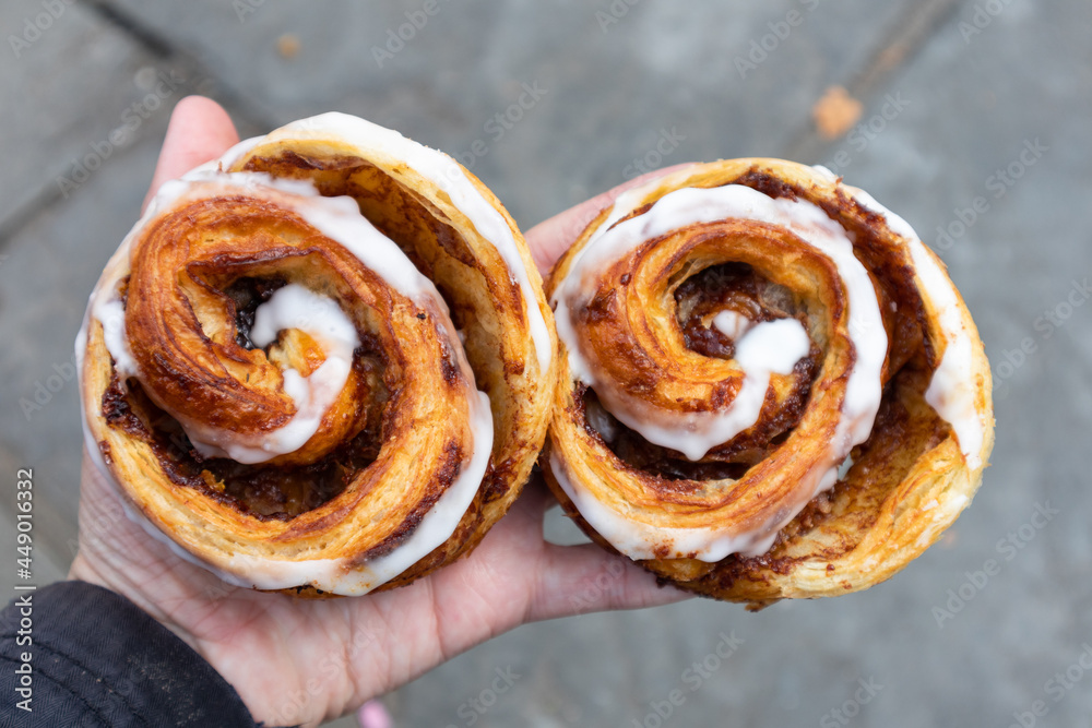 Fototapeta premium Two Delicious Cinnamon Rolls Held by a Hand