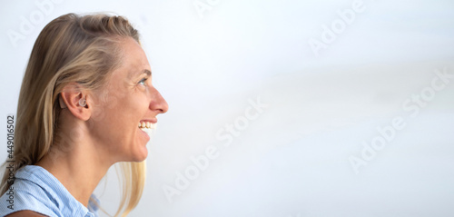 Woman's face in profile. Person wears beige colour hearing aid on ear. Problem with ear. Light background, space for text. Technology to hear well. Device for communication.