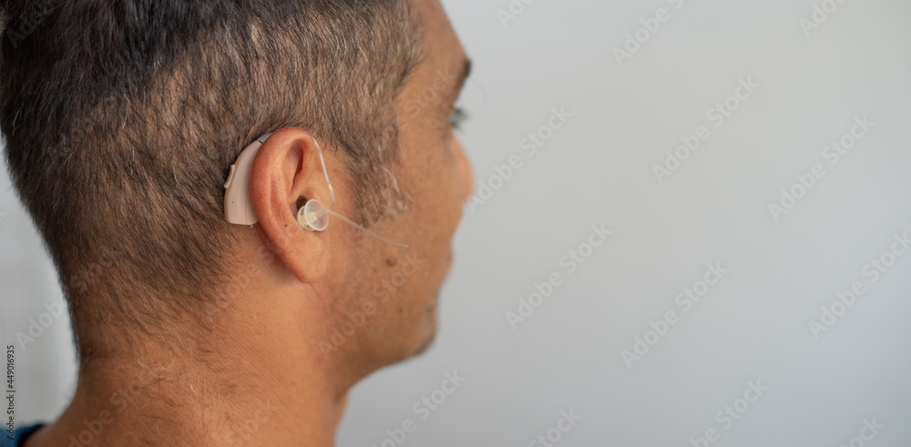 Man's face in profile. Person wears beige colour hearing aid on ear. Problem with ear. Light background, space for text. Technology to hear well. Device for communication. Man's face in profile. Person wears beige colour hearing aid on ear. Problem with ear. Light background, space for text. Technology to hear well. Device for communication.
