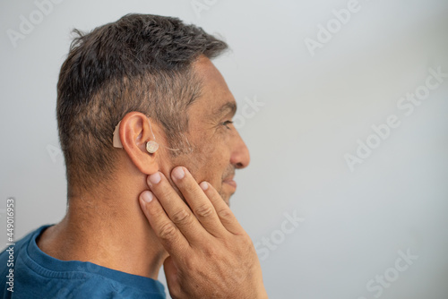 Man's face in profile. Person wears beige colour hearing aid on ear. Problem with ear. Light background, space for text. Technology to hear well. Equipment for communication