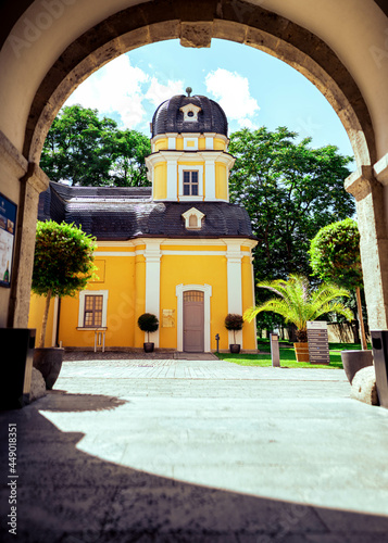 A bright yellow little church framed by an archway in front of a sunny blue sky