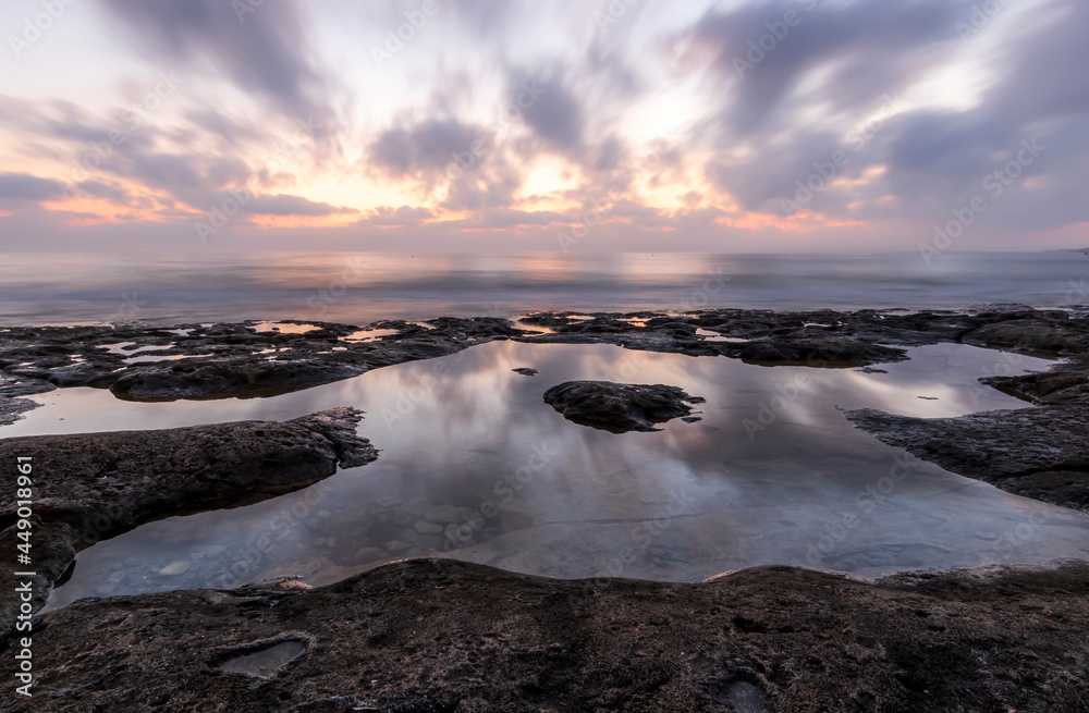 amazing scenic view at a sea shore from a coast after dramatic colorful sunset with flying blured clouds and reflection on water surface , beautiful ocean landscape