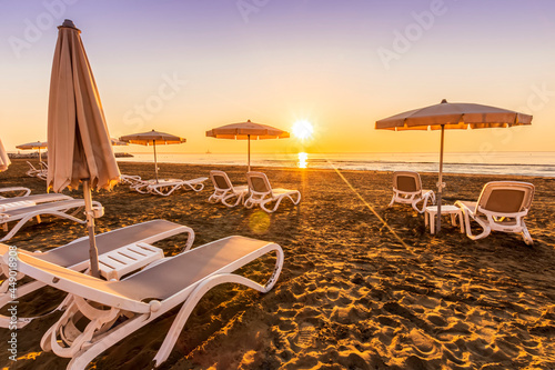 tranqiul sunrise an a beautiful beach with umbrellas on thr foreground , golden sand and sun rays and calm sea on the background photo