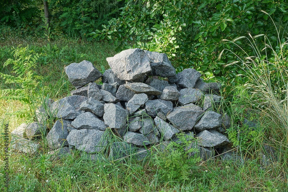 a big pile of gray stones on the street in green grass and vegetation