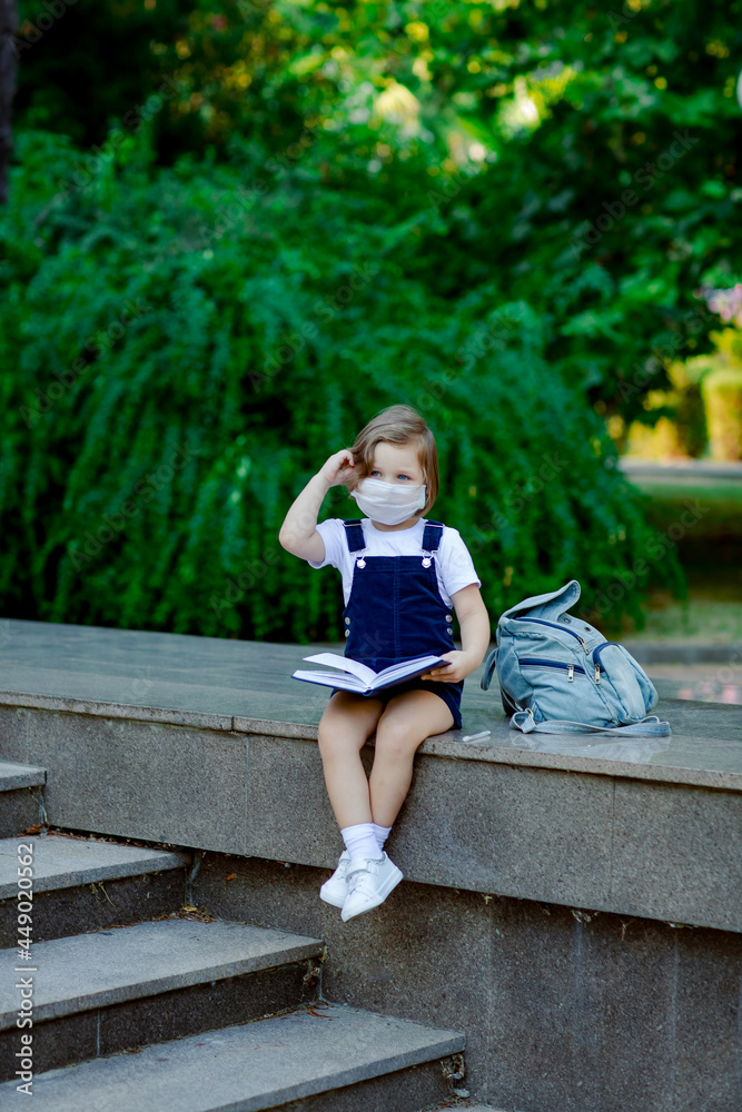 a little girl, a schoolgirl, sits outside the school during the day, a medical mask on her face a little girl, a schoolgirl, sits outside the school during the day, a medical mask on her face