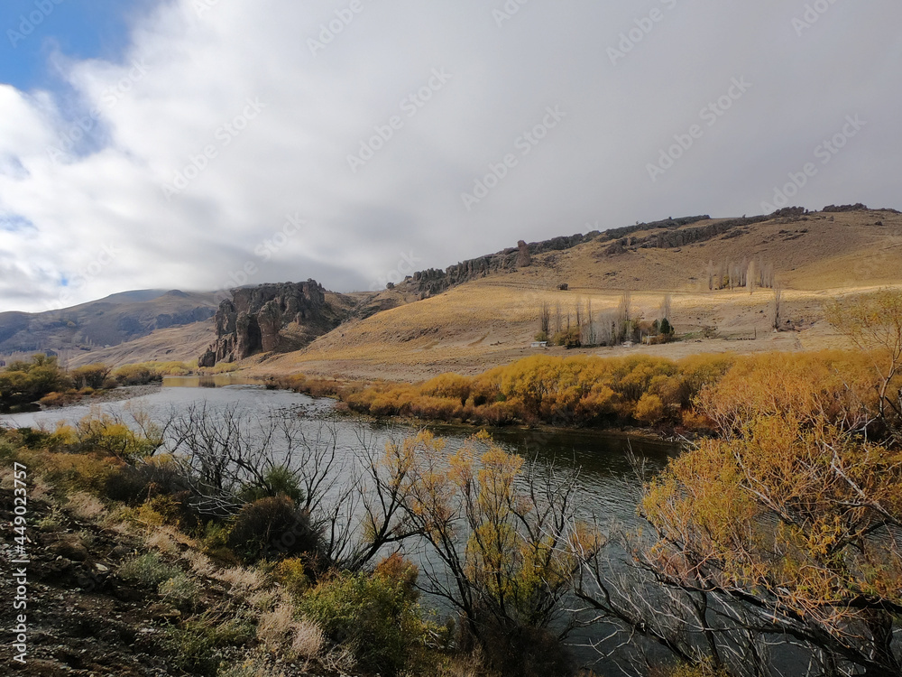 Idyllic alpine landscape. View of the river flowing across the golden valley and mountains. The pure water stream, yellow grassland, hills and rock formation in autumn.